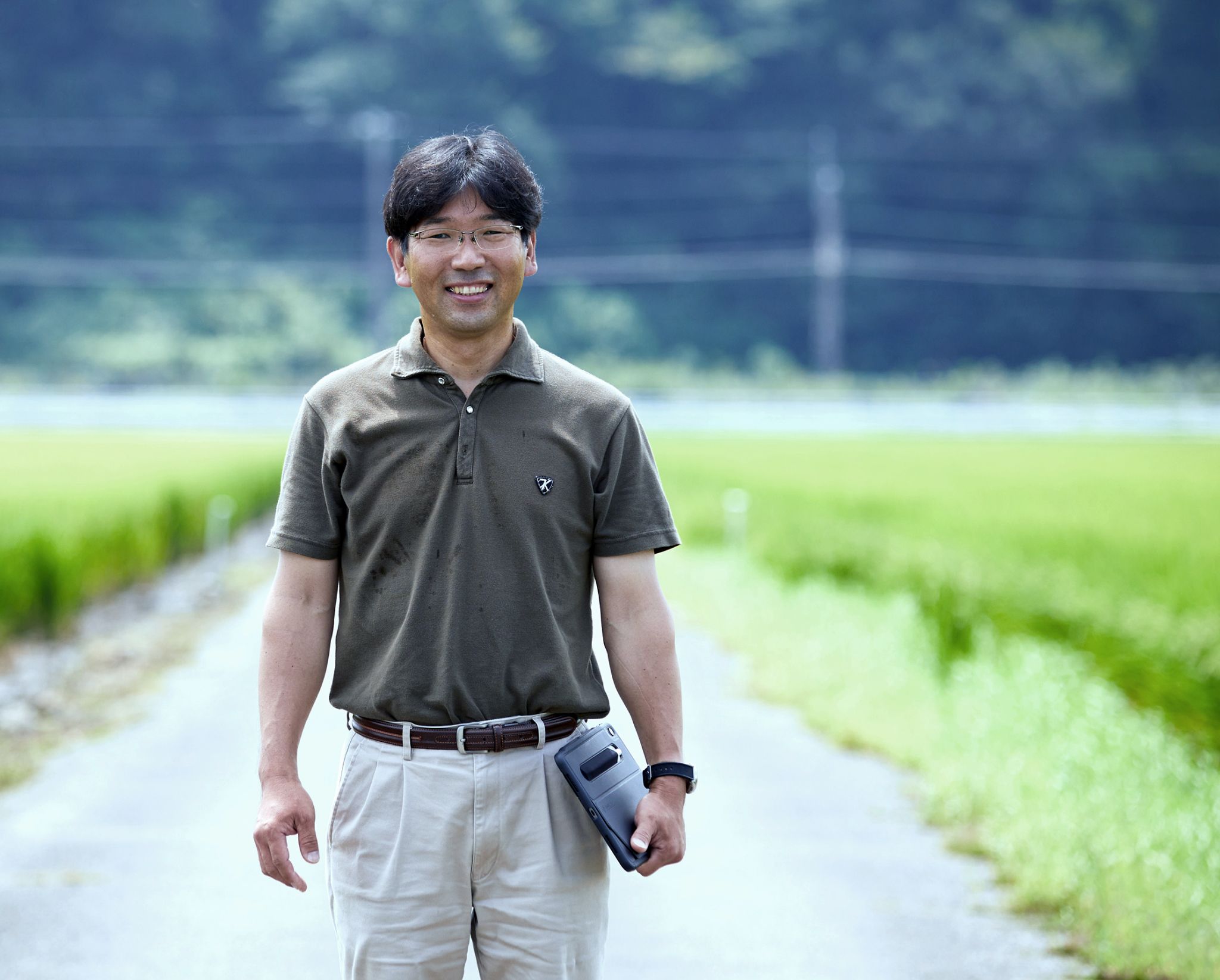 田圃道で正面を向いて立っている柔和な笑顔の井澤さん