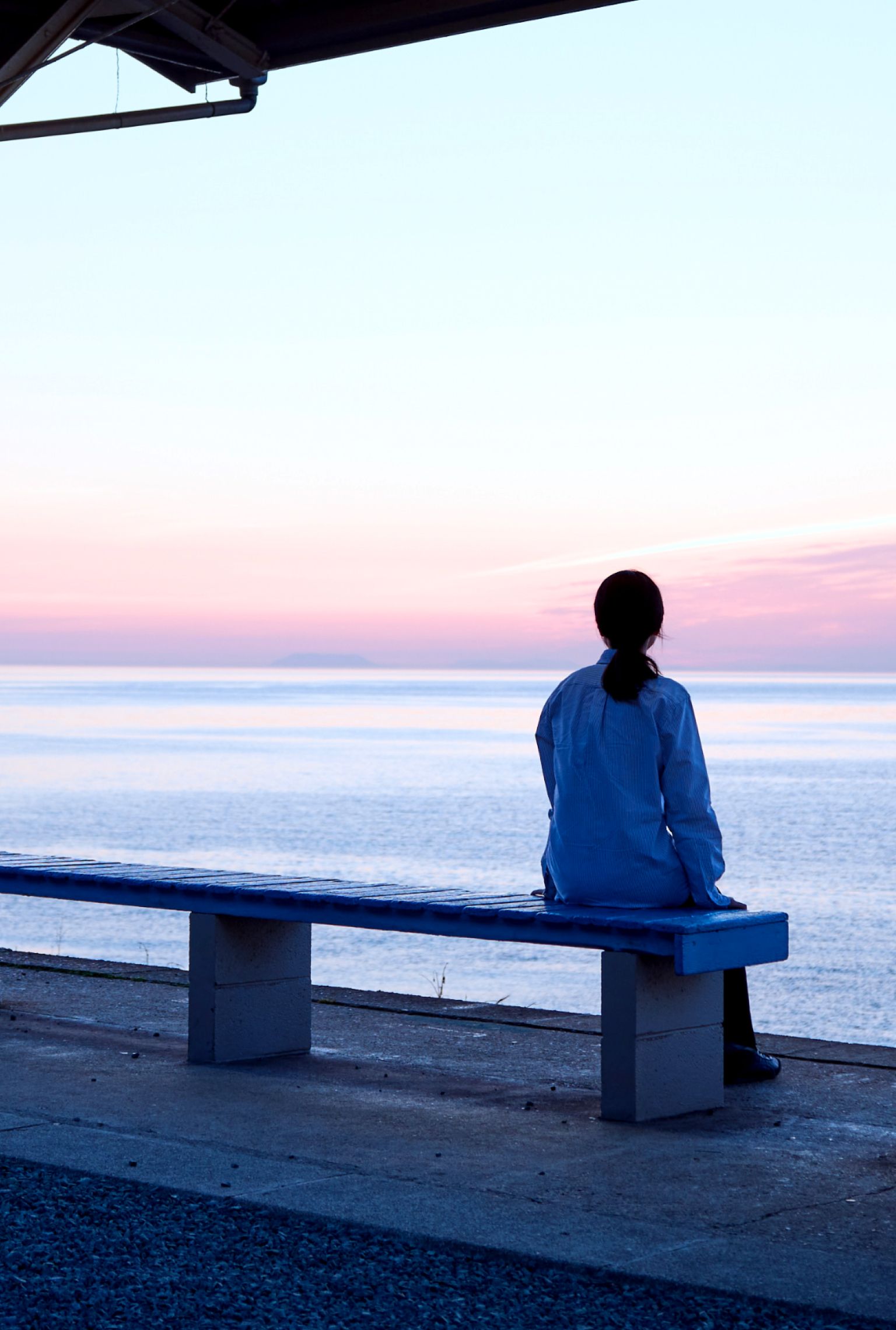 夕暮れに海の風を感じながらベンチに座っている女性