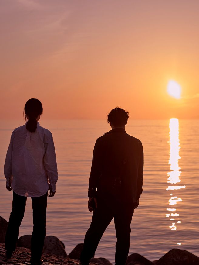 夕暮れ時に海辺で夕陽を見ている男性と女性