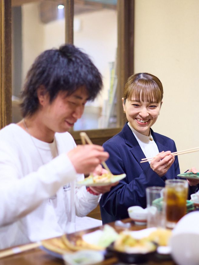 食事をしている男性と女性。男性はお皿を手に取りお箸で料理を掴もうとしている。女性をその様子を笑顔で見ている